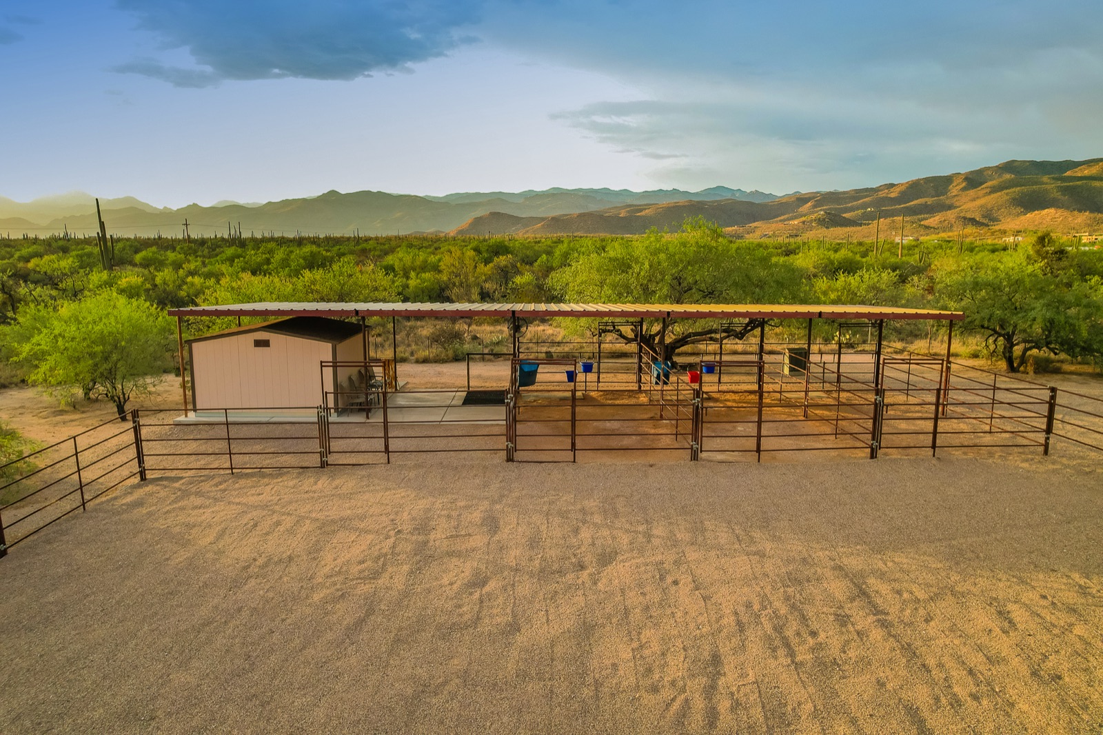 Covered horse stalls and pipe-rail turnouts at 2305 N El Camino Rinconado, with the Rincon Mountains behind